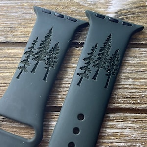 May include: Two dark green silicone Apple Watch bands with a laser-etched design of three pine trees.