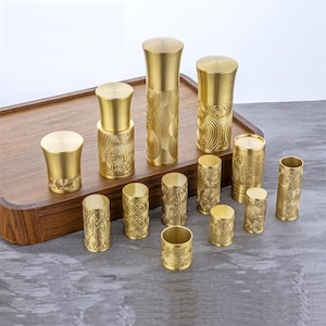 Pode incluir: Um conjunto de 12 rolhas de garrafa de metal dourado com um design de ondas. As rolhas estão dispostas sobre uma superfície de madeira.