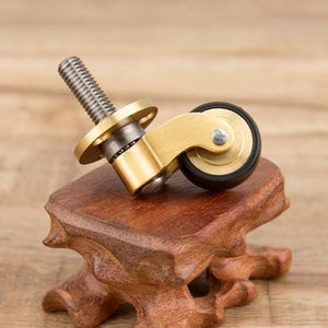 Puede incluir: Una rueda de giro de latón con una llanta de goma negra. La rueda tiene un eje roscado para sujetarlo a muebles u otros objetos.