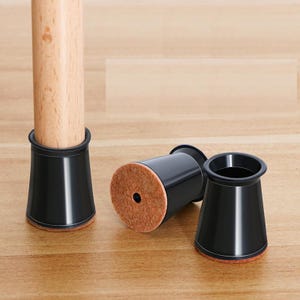 Puede incluir: Tres protectores de patas de muebles negros con almohadillas de fieltro marrón. Los protectores tienen forma de cono y un acabado liso y brillante.