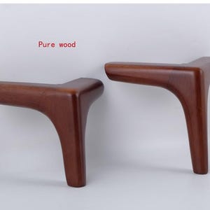 May include: Two wooden furniture legs in a light brown colour. The legs are shaped like an L and have a smooth finish. The text "Pure wood" is visible in the image.