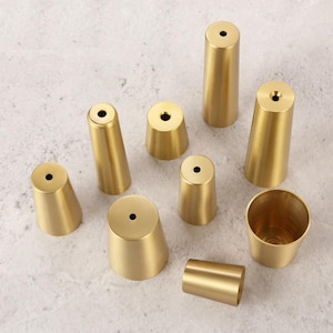 May include: A set of nine gold-toned metal furniture legs in various sizes and shapes. The legs are all cone-shaped and have a smooth, polished finish.