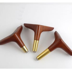 May include: Three wooden furniture legs with brass tips. The legs are shaped like a triangle with a rounded top and a flat bottom.
