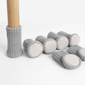 May include: Grey knitted furniture leg protectors with a non-slip felt pad on the bottom. The protectors are designed to prevent scratches and noise on hardwood floors.