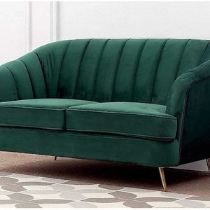 Puede incluir: Un sof&aacute; de terciopelo verde con respaldo capiton&eacute; y patas de metal dorado. El sof&aacute; est&aacute; sobre una alfombra estampada.