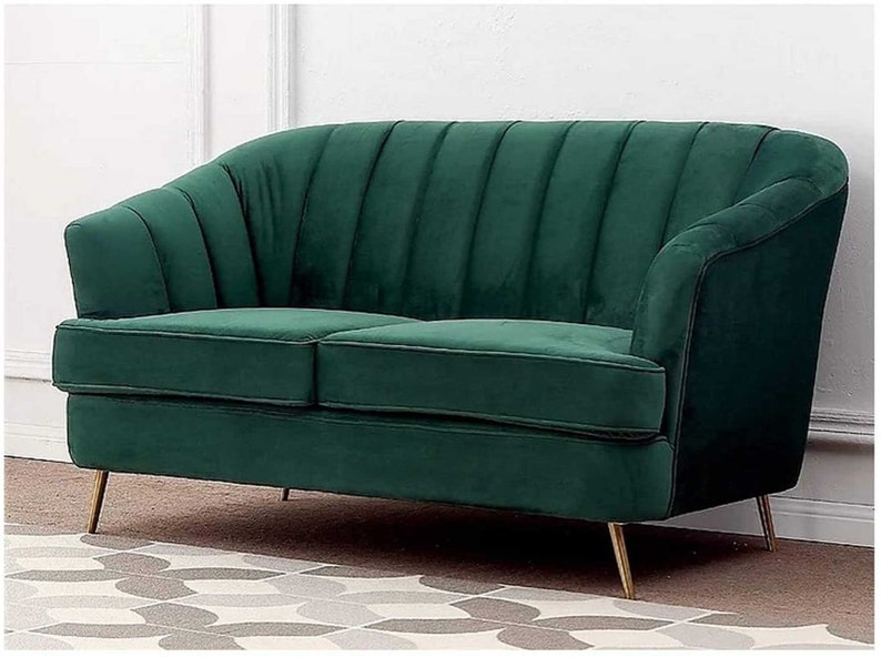Puede incluir: Un sof&aacute; de terciopelo verde con respaldo capiton&eacute; y patas de metal dorado. El sof&aacute; est&aacute; sobre una alfombra estampada.