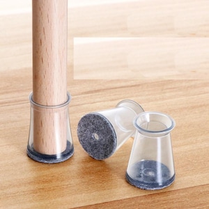 Könnte beinhalten: Drei transparente Möbelbein-Schutzkappen aus Kunststoff mit grauen Filzpads. Die Schutzkappen sind so konzipiert, dass sie Kratzer auf Böden verhindern.