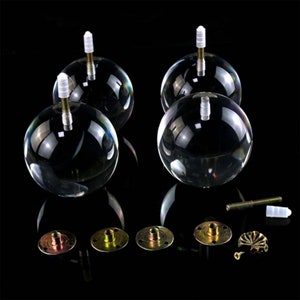 Puede incluir: Cuatro patas de muebles de acrílico transparente con base de metal y tornillos. Las patas son redondas y tienen un acabado brillante. La base de metal es de color dorado y tiene una superficie plana. Los tornillos son de color plateado y tienen cabeza Phillips.