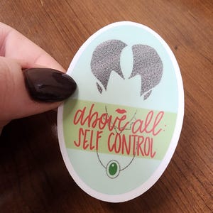 May include: A light blue and green oval sticker with a silver silhouette of a woman's head. The sticker has the text "above all: self control" in red and black lettering.