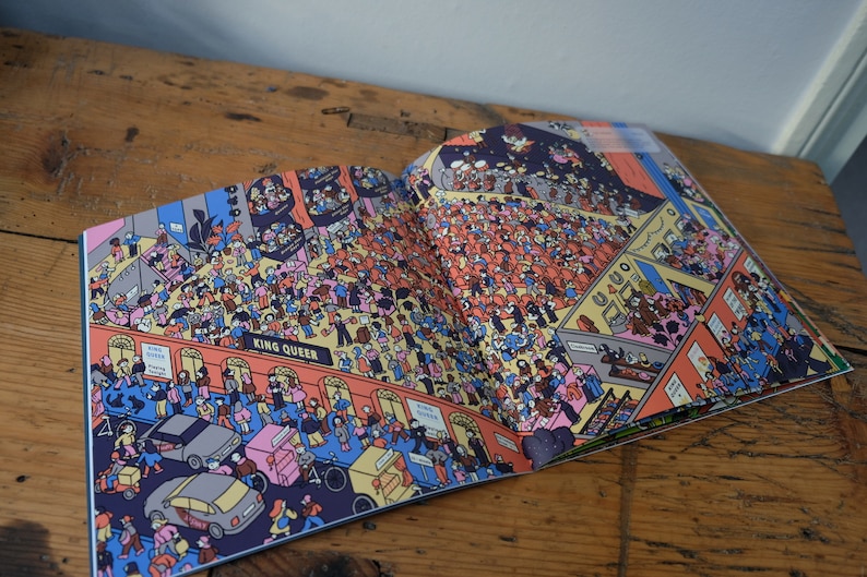 Może przedstawiać: Otwarta książka z kolorową ilustracją zatłoczonego pokoju. Ilustracja jest pełna ludzi, samochod&oacute;w i budynk&oacute;w. Na książce widoczny jest tekst "King Queen".