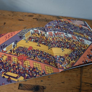 Może przedstawiać: Otwarta książka z kolorową ilustracją zatłoczonej sceny. Ilustracja jest pełna ludzi, budynk&oacute;w i drzew. Książka jest otwarta na stronie z tekstem "SS21" na budynku.