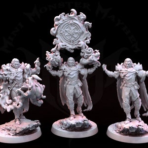 Puede incluir: Tres figuras en miniatura de magos, cada una con una túnica fluida y un bastón, de pie sobre bases circulares. Las figuras están pintadas en color gris claro. Un símbolo circular con llamas está suspendido sobre las figuras.