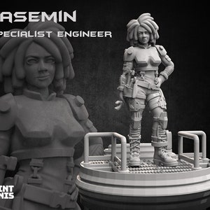May include: A grey 3D printed miniature of a female figure with short, spiky hair. She is wearing a futuristic outfit with a tool belt and boots. The figure is standing on a round base. The text "YASEMIN SPECIALIST ENGINEER" is printed above the figure.
