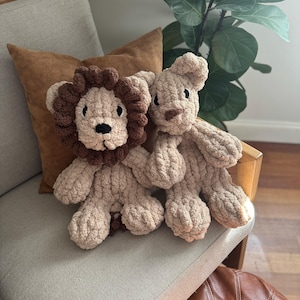 Puede incluir: Dos juguetes de peluche de le&oacute;n hechos a mano. Un le&oacute;n tiene una melena marr&oacute;n y el otro una cabeza simple. Ambos son beige y tienen ojos y narices negros. Est&aacute;n sentados en una silla gris claro con un coj&iacute;n marr&oacute;n.