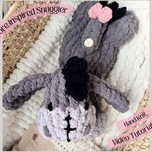 Può includere: Un giocattolo coccoloso fatto a mano ispirato a Eeyore, grigio e nero. Il peluche presenta dettagli rosa e un bottone. È presente anche il testo "Mini Eeyore Inspired Snuggler" e "Hand Knit Video Tutorial & PDF".