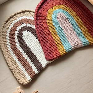 May include: Two crocheted rainbow rugs in different color combinations. The rug on the left is beige, brown, white, and dark brown. The rug on the right is red, orange, yellow, light blue, and pink.