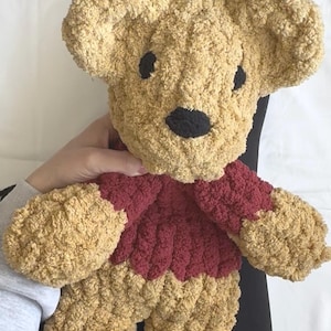Puede incluir: Un oso de peluche hecho a mano, con un cuerpo y una cabeza de color marr&oacute;n claro texturizado. El oso tiene un su&eacute;ter rojo oscuro y ojos y nariz negros. El juguete blando est&aacute; dise&ntilde;ado con orejas y extremidades grandes y redondeadas.