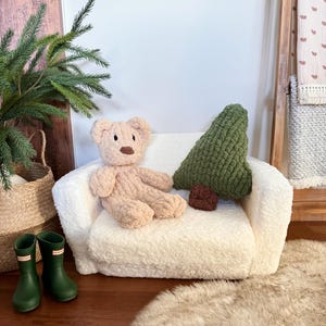 Puede incluir: Un peque&ntilde;o sof&aacute; de felpa color crema con un oso de peluche y una almohada verde en forma de &aacute;rbol. Tambi&eacute;n se ven una almohada redonda marr&oacute;n y un par de botas de agua verdes. El sof&aacute; est&aacute; sobre una alfombra de piel sint&eacute;tica.