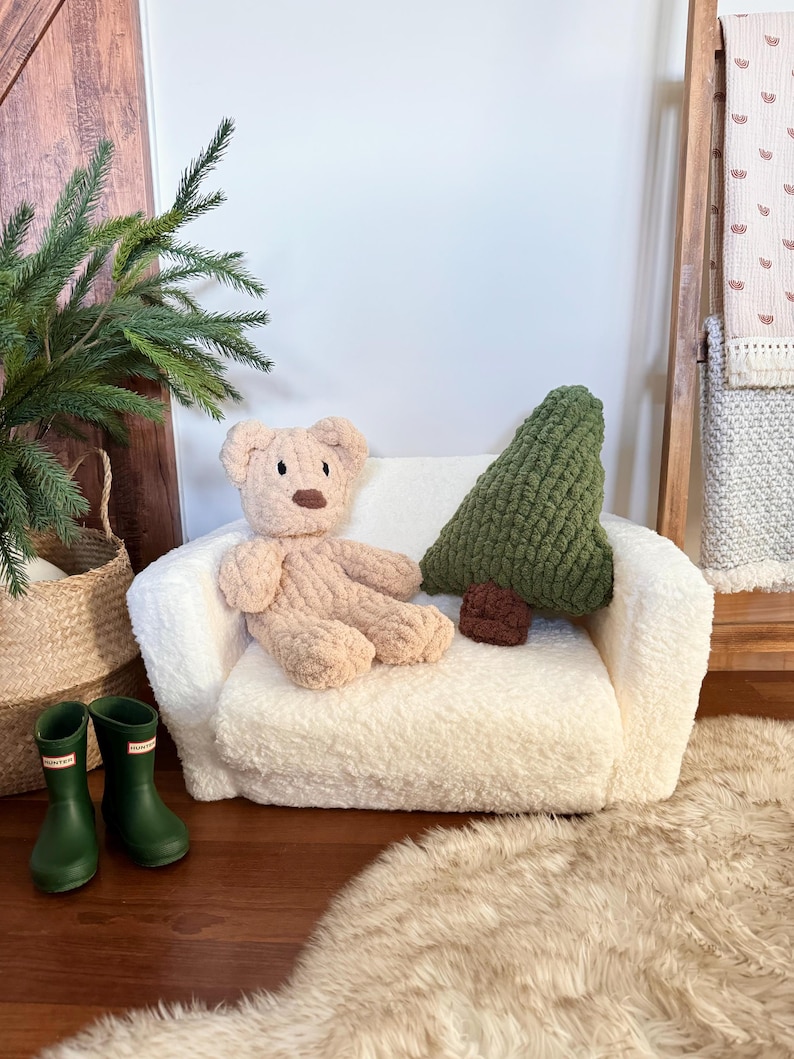 Puede incluir: Un peque&ntilde;o sof&aacute; de felpa color crema con un oso de peluche y una almohada verde en forma de &aacute;rbol. Tambi&eacute;n se ven una almohada redonda marr&oacute;n y un par de botas de agua verdes. El sof&aacute; est&aacute; sobre una alfombra de piel sint&eacute;tica.