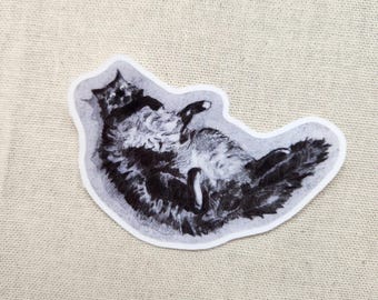Könnte beinhalten: Ein schwarz-weißer Aufkleber einer Katze, die auf dem Rücken liegt. Die Katze ist in einem detaillierten, skizzenartigen Stil gezeichnet, mit sichtbarer Fellstruktur. Der Aufkleber hat einen weißen Rand und befindet sich auf einer beigefarbenen Stoffoberfläche.