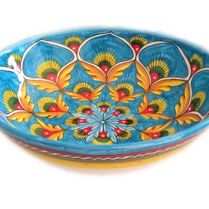Può includere: Una grande ciotola rotonda in ceramica blu con un bordo giallo e intricati disegni floreali colorati. La ciotola presenta un motivo ripetitivo di foglie e fiori gialli, rossi e verdi.