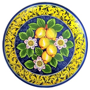 Może przedstawiać: Niebieski i żółty talerz ceramiczny z kwiatowym wzorem przedstawiającym cytryny i kwiaty. Talerz ma ozdobną ramkę z żółtym tłem i czarnymi spiralami.