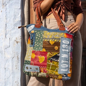 Può includere: Una grande borsa tote in patchwork con una base in denim blu e toppe di tessuto colorate. La borsa ha un manico in pelle marrone e una toppa bianca con il testo "LOT N 180" sul davanti.