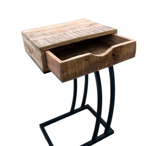 May include: A wooden side table with a drawer, featuring a natural wood finish and a black metal base. The drawer is partially open, revealing the interior. The table's design is modern and functional, suitable for a living room or bedroom.