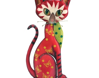 Può includere: Figurina di gatto in metallo rosso con una sciarpa verde e bianca, pois gialli e motivi a farfalla. Il gatto è seduto su un supporto in metallo nero.