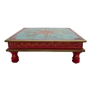 May include: A square wooden table with hand-painted floral designs in gold, red, and blue on a teal background. The table has four red legs with a decorative design.