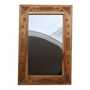 Peut inclure: Miroir rectangulaire en bois avec un cadre marron clair. Le cadre présente des motifs découpés complexes en forme de losanges et d'étoiles. Le miroir reflète une surface blanche et un fond sombre.