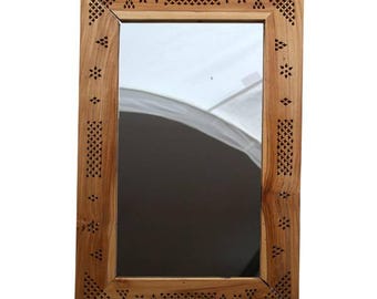 May include: Rectangular wooden mirror with a light brown frame. The frame has intricate cut-out patterns of diamonds and star shapes. The mirror reflects a white surface and a dark background.