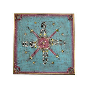 May include: A square wooden box with a blue background and a hand-painted design in yellow, pink, and white. The design features a central flower with four stylized arrows radiating outward.