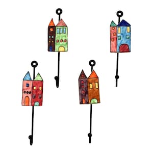 Op de afbeelding: Set van vier keramische haken in de vorm van huizen in verschillende kleuren, waaronder rood, blauw, groen en bruin. Elke haak heeft een zwarte metalen steel.