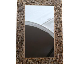 Peut inclure: Miroir rectangulaire avec un cadre à motifs géométriques. Le cadre présente un motif de cubes répétitifs dans des tons de marron et de noir. Le miroir reflète une lumière blanche vive.