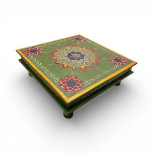 Könnte beinhalten: Ein quadratischer, dekorativer Holztisch mit einer grün lackierten Oberfläche. Der Tisch hat ein Blumendesign in der Mitte und an jeder Ecke, mit roten, gelben und schwarzen Akzenten. Die Kanten sind mit Goldfarbe verziert. Der Tisch wird von vier kurzen, abgerundeten Beinen getragen.