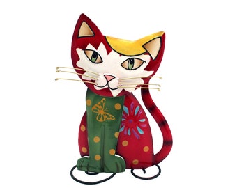 Può includere: Figurina decorativa a forma di gatto in metallo. Il gatto è principalmente rosso con accenti gialli, bianchi e verdi. Ha una sciarpa verde con un disegno di farfalla gialla e baffi dorati. Il gatto è seduto in posizione eretta con un design stravagante.