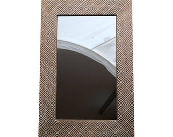 Peut inclure: Miroir rectangulaire avec un motif géométrique en losanges sculpté dans le cadre en bois. Le cadre est de couleur marron clair et le miroir reflète l'environnement. Le miroir est un objet décoratif.