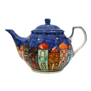 Può includere: Una teiera in ceramica blu con un design a notte stellata e case colorate dipinte sul lato.