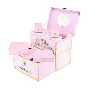Puede incluir: Un calendario de adviento de belleza rosa con detalles dorados y un espejo en forma de corazón dentro de la tapa. El calendario abierto revela cajas numeradas. El texto "Beauty Advent Calendar" es visible, junto con la marca "bubble".