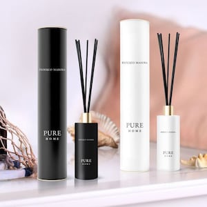 May include: Two reed diffusers and their cylindrical packaging are displayed. One set is black with gold accents, the other is white. The text "FEDERICO MAHARA" and "PURE HOME" are printed on the packaging and bottles.