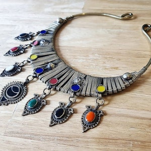 May include: A silver choker necklace with a decorative band of metal and colorful enamel accents. The necklace has several dangling charms with enamel accents in various colors.
