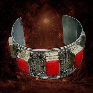 May include: Silver-toned cuff bracelet with ornate detailing and five rectangular red stone inlays. The bracelet has a wide band and an open design. The background is a dark, textured gradient.