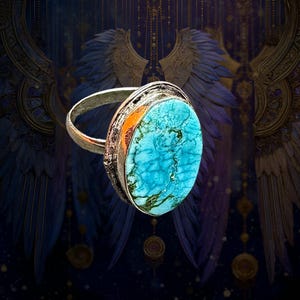 May include: A silver-toned ring featuring a large, oval-shaped turquoise stone with prominent dark veining. The metal band has a textured, weathered appearance, and the stone is set within a simple, polished silver-colored bezel setting.