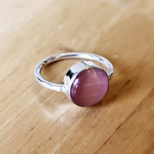 May include: A silver ring featuring a pink gemstone. The ring is simple and elegant.