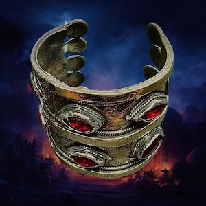May include: A wide, antique-style cuff bracelet with a silver finish. The bracelet features three rows of red, oval-shaped stones and intricate etched designs. The top and bottom edges have a decorative, raised design.