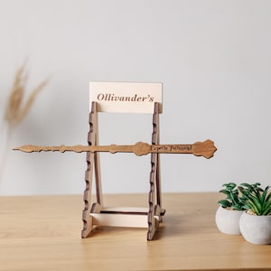 以下が含まれることがあります： Ollivander'sと書かれた看板が付いた明るい色の木製ディスプレイスタンド。Expecto Patronumという文字が刻印された水平の茶色の木製ワンドを保持しています。スタンドにはワンドを固定するための切り込みが入った側面サポートがあります。