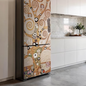 May include: A refrigerator with a decorative wrap featuring a tree design in shades of gold, brown, and cream. The artwork includes swirling patterns, geometric shapes, and an owl. The fridge has a black handle and is set against a white kitchen.