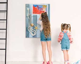 May include: Two children are hanging a framed artwork on a wall. The artwork features a blue and white striped background with a rope, seashells, and a starfish. The artwork also includes a red and white drawing of a fish.