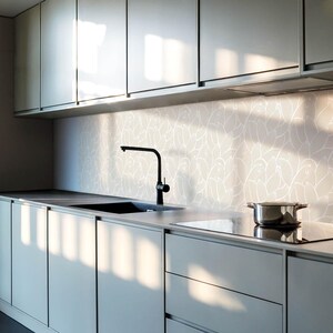Puede incluir: Una cocina moderna con armarios gris mate de puertas lisas, un grifo negro de cuello de cisne y una olla de acero inoxidable sobre la placa de cocina. El salpicadero muestra un patrón repetitivo blanco y gris claro de plumas de ave.